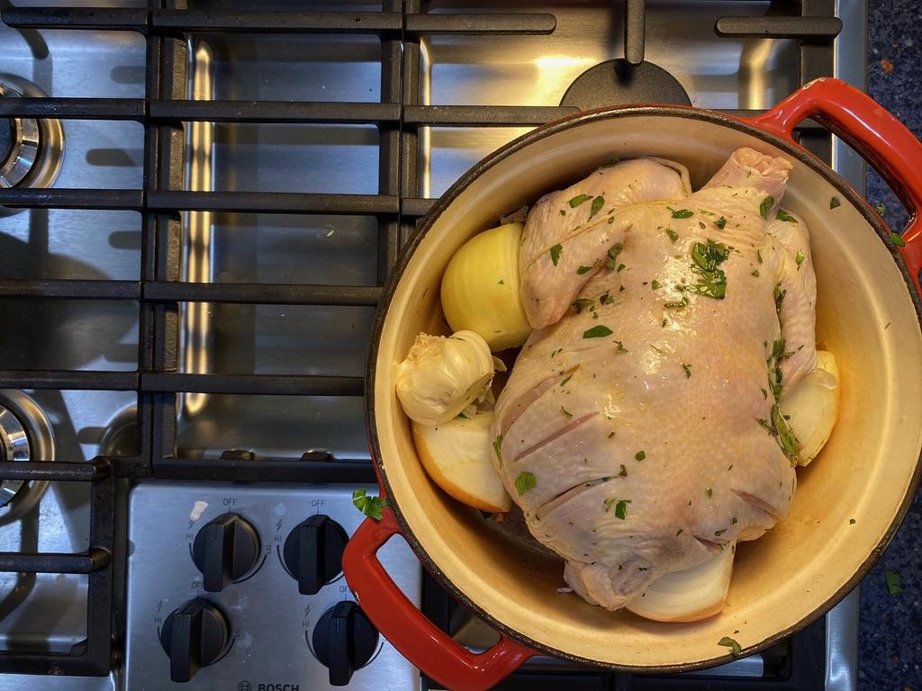 A photo of the top of the thrice-aforementioned chicken, in a pot with herbs and lemon and onion, but this time on the stove.
