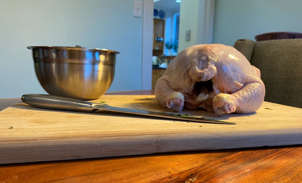 A photo of the back of an uncooked chicken, a mixing bowl, and a knife on the cutting board from before.