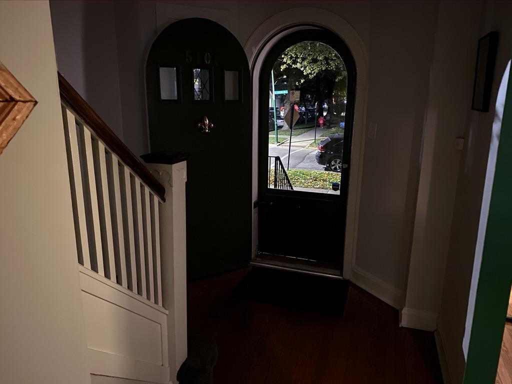 A photo of the front door of a house, taken from the vantage point of the second floor. The house is dark, the lighting dim and lonesome.